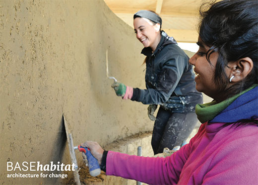 Two women from diverse cultural backgrounds in the process of jointly plastering a curved earth plaster wall